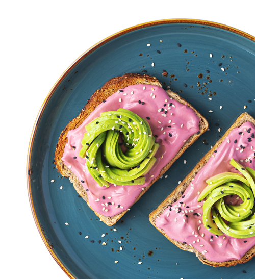 Open-faced toast with beet spread and avocado sliced whirls sprinkled with hemp seeds