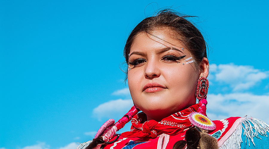 Photograph of a proud indigenous woman with beads in front of a clear blue sky