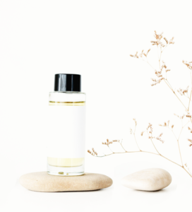 bottle of essential oil on a beige stone, next to another stone with some baby's breath