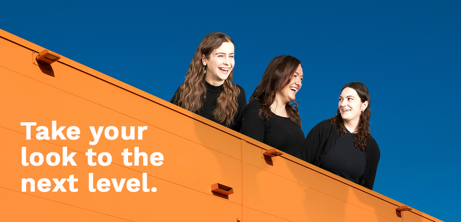 Photograph of Alexis, Christel and Jada laughing on top of an orange building with a clear dark blue sky behind them. Copy that reads: Take your look to the next level.